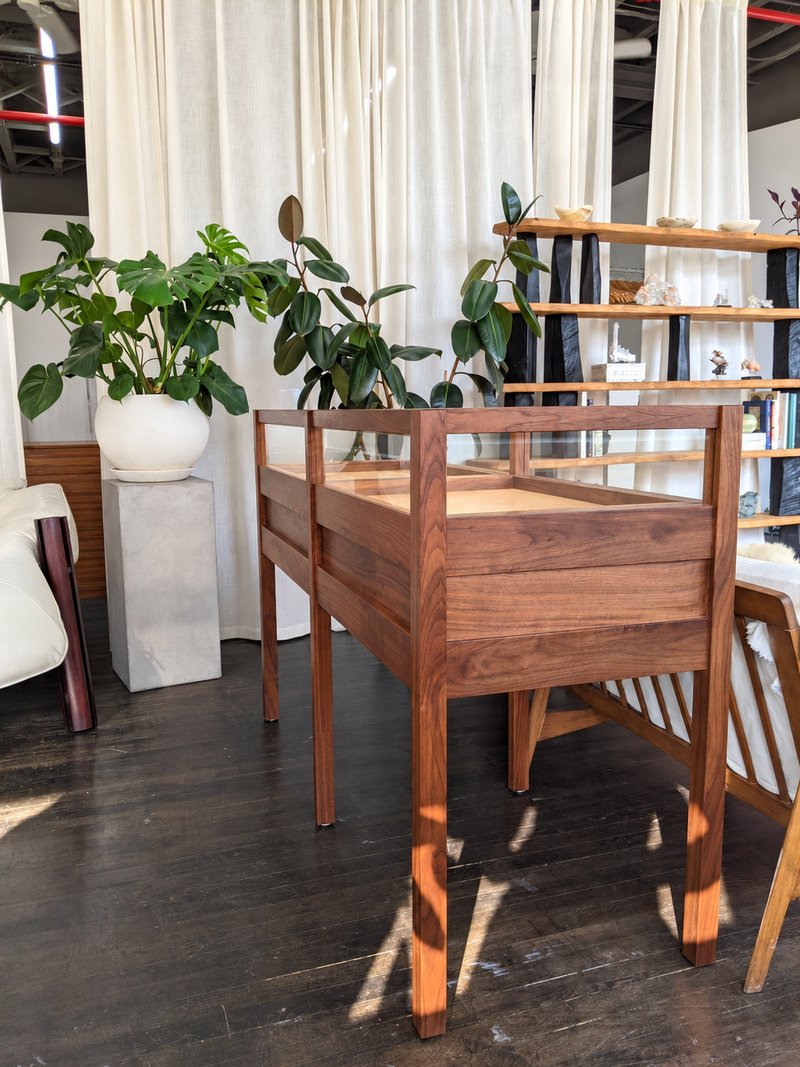 Side view of a walnut display case showing the glass enclosure, wooden drawer fronts, and tall legs.
