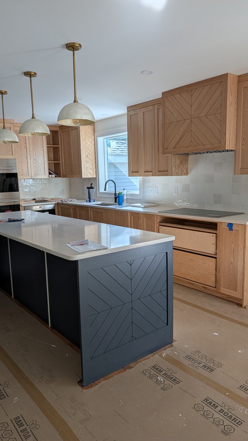Custom patterned painted island panel and red oak range hood panel during kitchen installation.